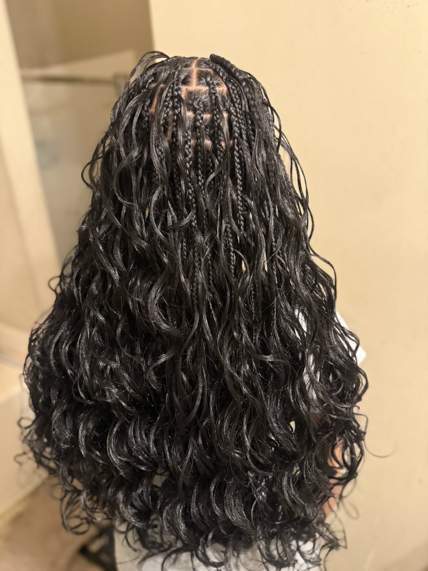 Boho knotless braids with curly ends, seen from behind against a white wall