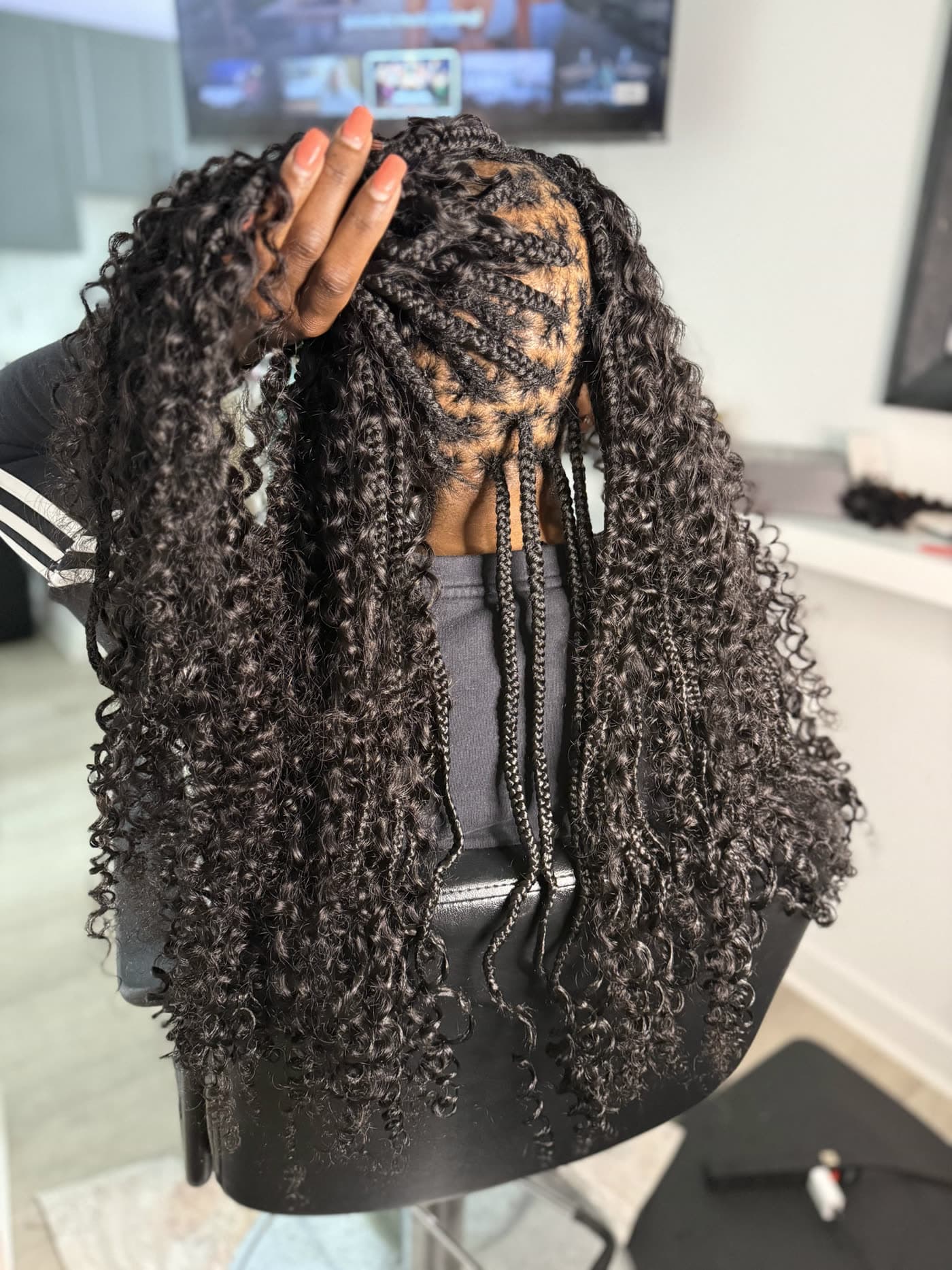 A hand lifting a full head of boho knotless braids with curly ends